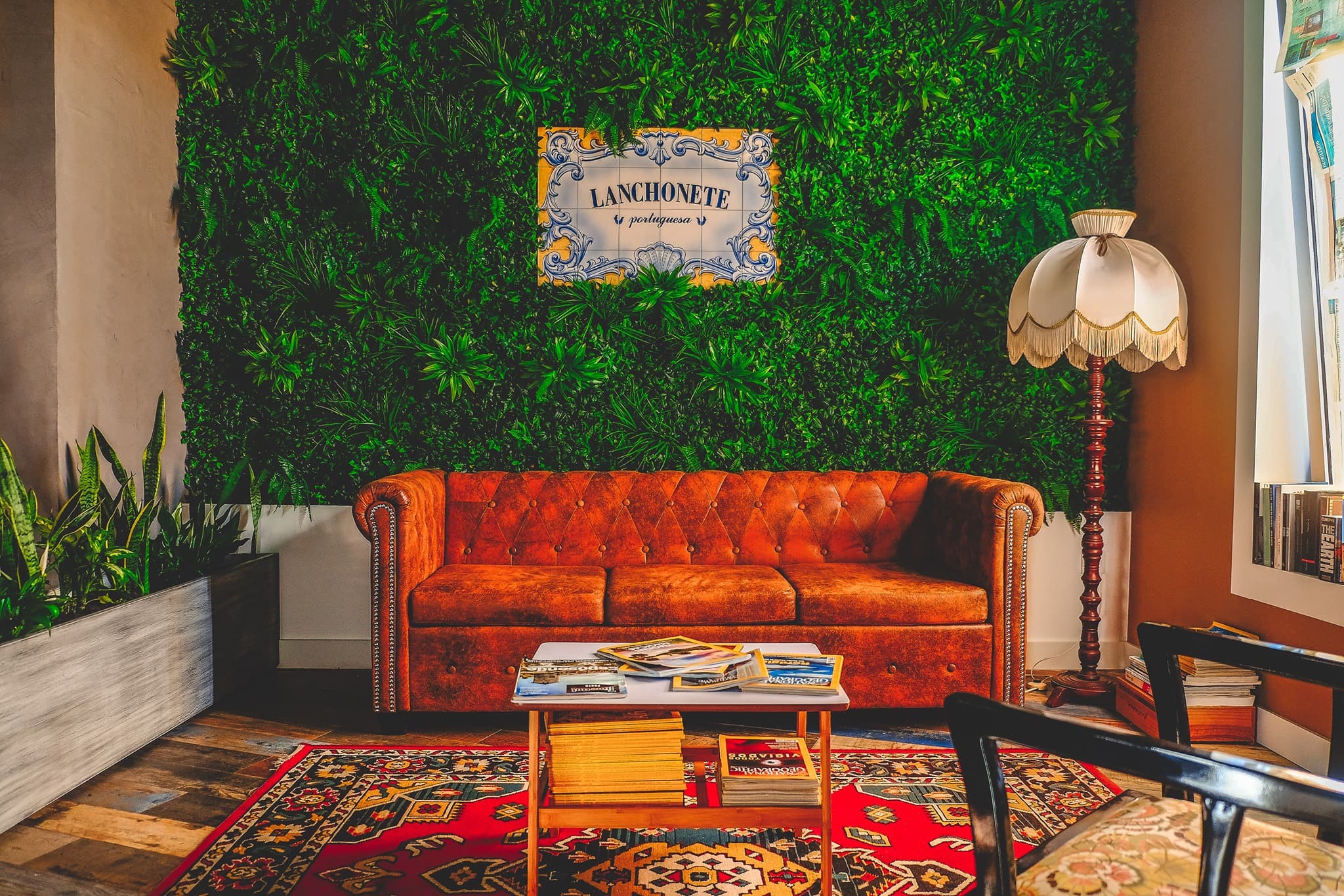 Entrada da Lanchonete Portuguesa com parede verde, sofá de couro castanho e candeeiro vintage.